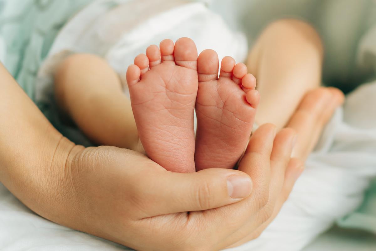 Pés delicados de recém-nascido em posição natural, acolhidos por mãos adultas em close-up humano e terno